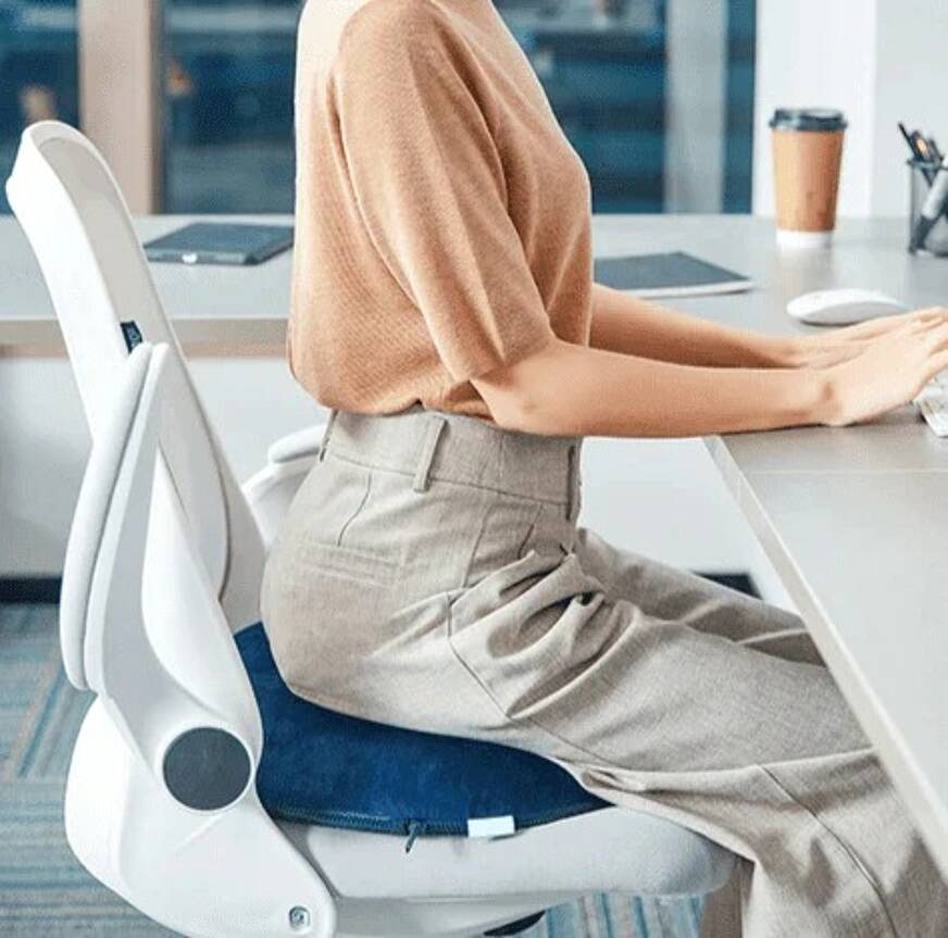Imagem de uma pessoa sentada na cadeira de trabalho, sobre um travesseiro ortopédico para cóccix.